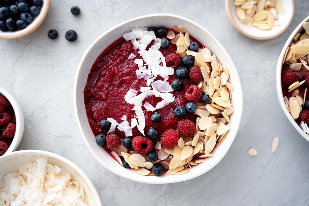 Berry smoothie bowl topped with fresh blueberries, raspberries, coconut flakes, and sliced almonds.